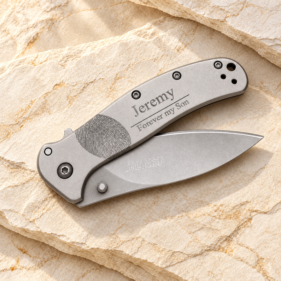 Exact knife and partially open blade laid diagonally across warm cream stone, entire knife fits with generous margins. Preserve engraving Jeremy / Forever my Son and Kershaw mark.