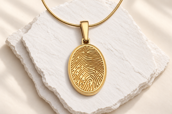 Gold oval fingerprint necklace framed larger on white slate.